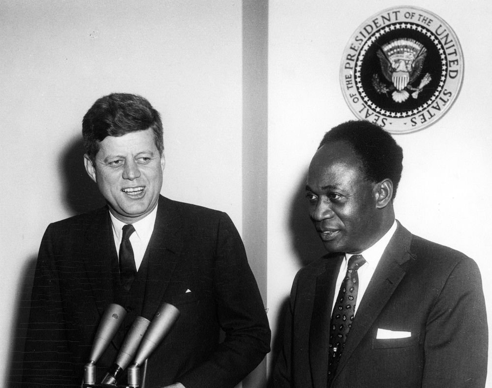 Kwame Nkrumah at right stands beside John F. Kennedy behind microphones in a black-and-white photograph.