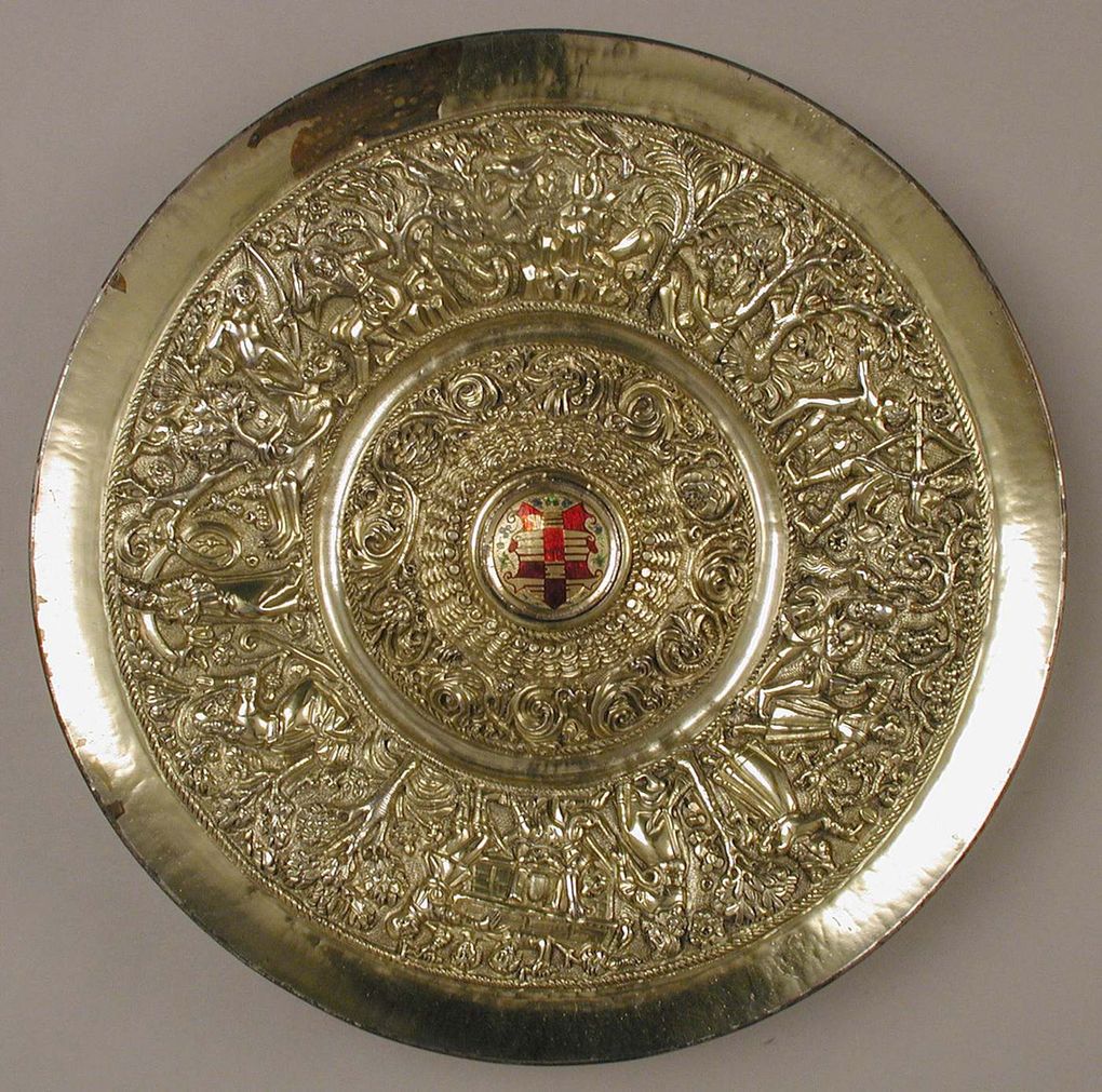 A round gilded plate with intricate ornament and a central coat of arms.