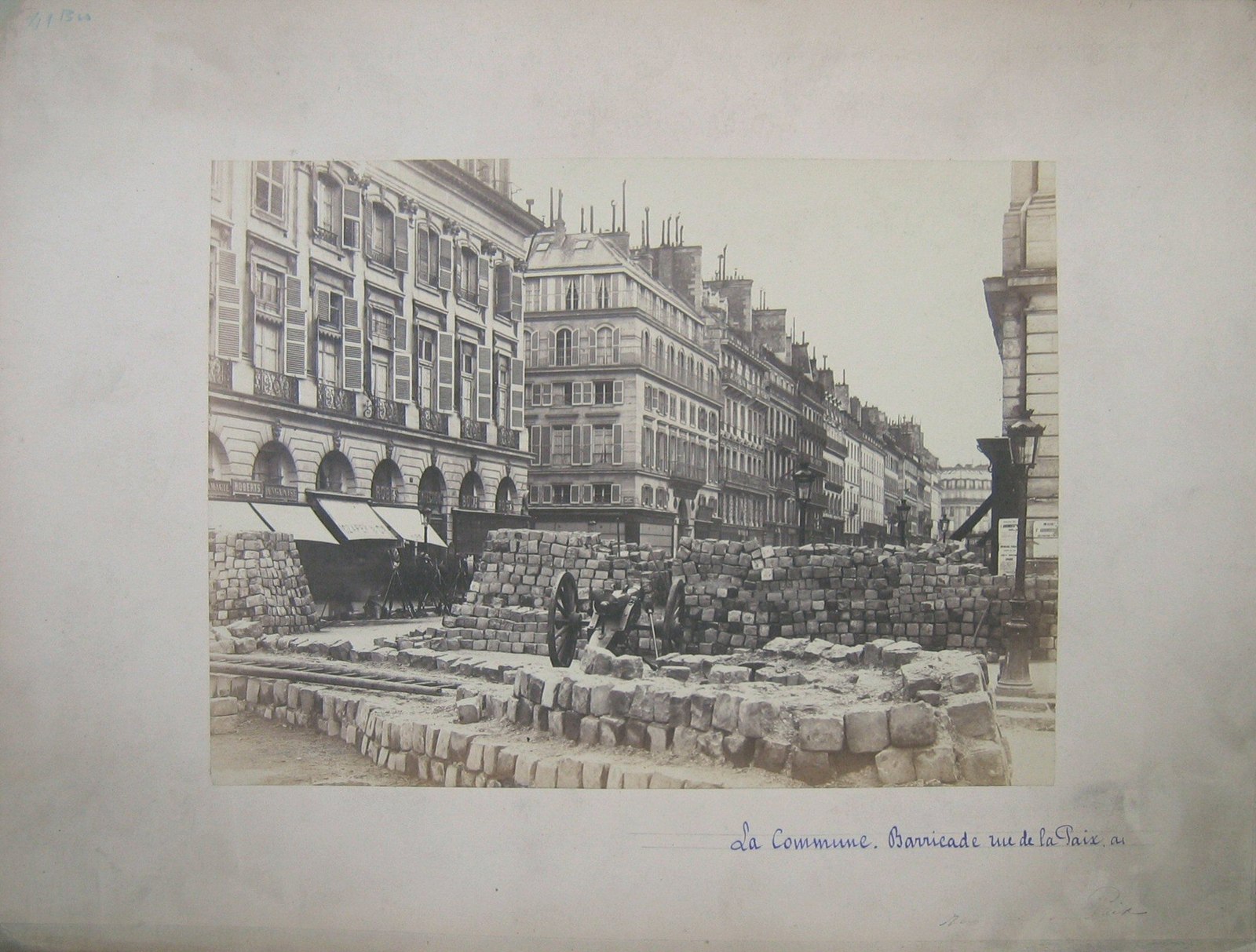Fotografía del siglo XIX, con su montaje, de una barricada de piedra y un cañón en la rue de la Paix, con edificios de París al fondo.
